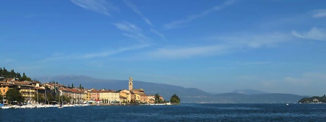 Trip Islands beliebte Urlaubsziele am Gardasee -  Mit einer Fläche von 370 km² ist der Gardasee der größte See Italiens. Es liegt am Fuße der Alpen und erstreckt sich über drei Staaten: Lombardei, Venetien und Trentino. Die maximale Tiefe des Sees beträgt 346 m, er hat eine längliche Form und sein nördliches Ende ist sehr schmal. Dort ist der See von den Bergen der Gruppo di Baldo umgeben. Du trittst aus deinem gemütlichen Hotelzimmer und es begrüßt dich die warme italienische Sonne. Du blickst auf den atemberaubenden Gardasee, der in zahlreichen Blautönen schimmert - von tiefem Dunkelblau bis zu funkelndem Türkis. Majestätische Berge umgeben dich, während die Brise sanft deine Haut streichelt und der Duft von blühenden Zitronenbäumen deine Nase kitzelt. Du schlenderst die malerischen, engen Gassen entlang, vorbei an farbenfrohen, blumengeschmückten Häusern. Vereinzelt unterbricht das fröhliche Lachen der Einheimischen die friedvolle Stille. Du fühlst dich wie in einem Traum, der nicht enden will. Jeder Schritt führt dich zu neuen Entdeckungen und Abenteuern. Du probierst die köstliche italienische Küche mit ihren frischen Zutaten und verführerischen Aromen. Die Sonne geht langsam unter und taucht den Himmel in ein leuchtendes Orange-rot - ein spektakulärer Anblick.
